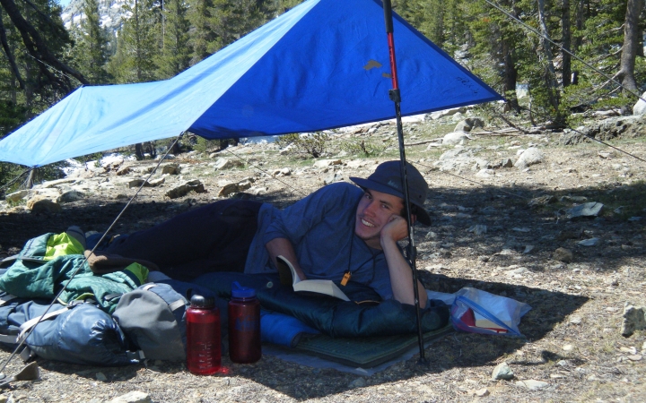 a person smiles while resting under a tarp shelter
